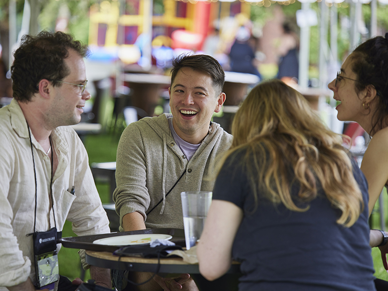 Four alumni sit at a table outside, eating and talking during Reed College’s Reunions.