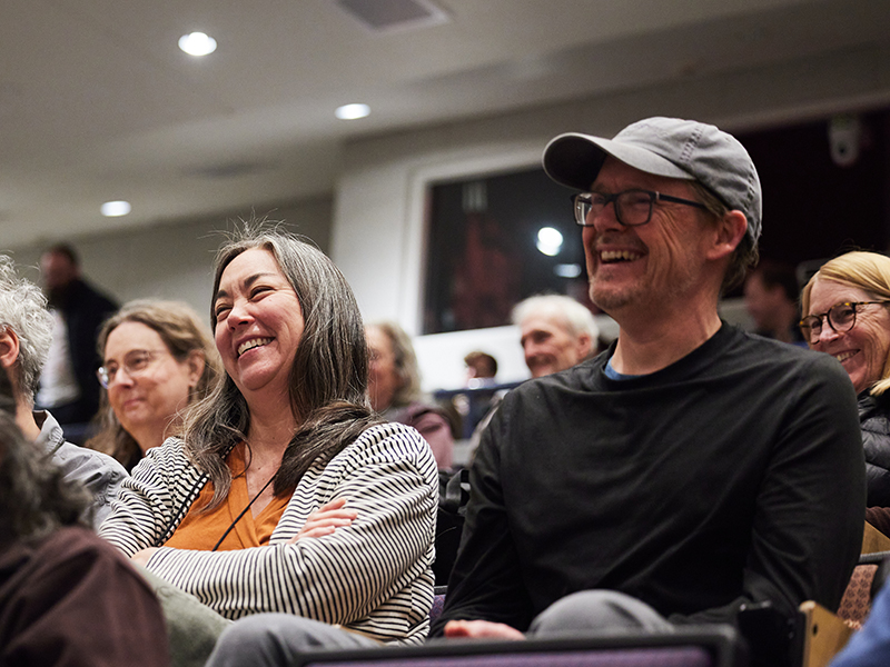 A group of alumni sitting in Vollum Lecture Hall laughing and smiling during an Alumni College presentation.