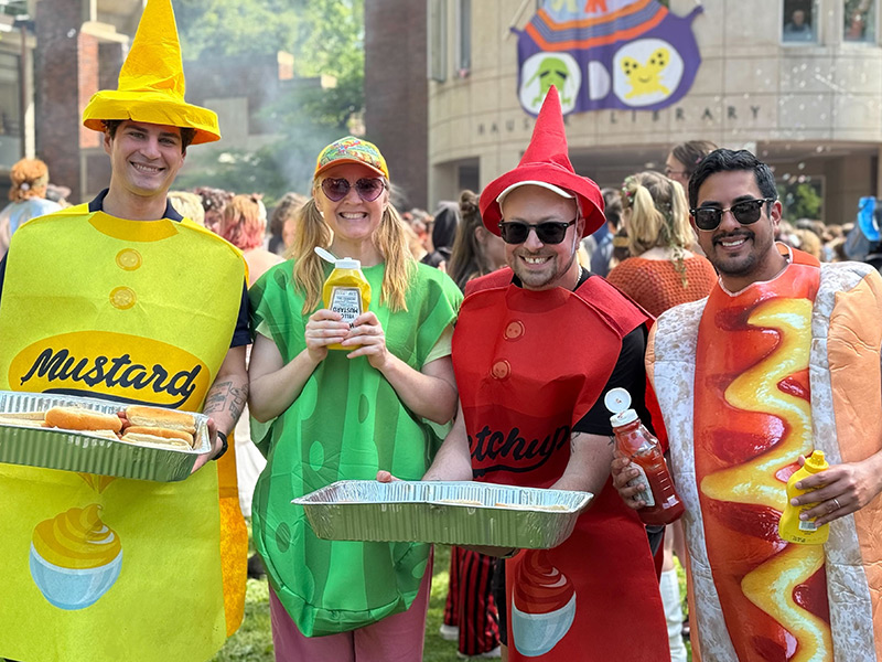 Four Reed staff members in condiment costumes serving hot dogs during thesis parade.