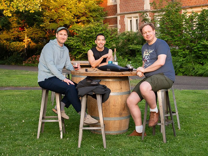 Three Reed alumni seated at a barrel table in the quad during Reunions.