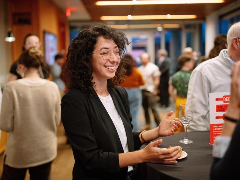 A person smiles and gestures with their hands while talking to other attendees at Reedies Drink Wine for Reed.