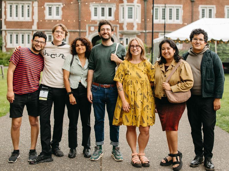 A group of young Reed alumni, arm in arm in the Quad at Reunions, smile for the camera.