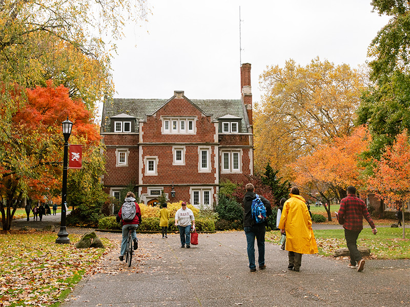 An autumn scene in front of Old Dorm Block with students passing the leaf-covered sidewalk.