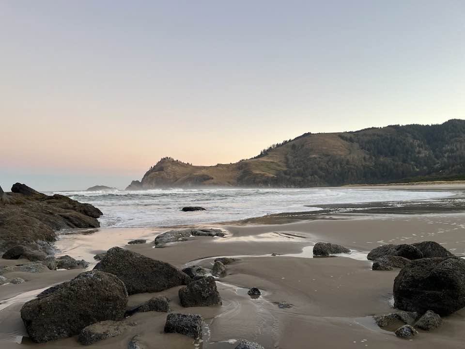 Image of sandy beach with large rocks at dusk. 