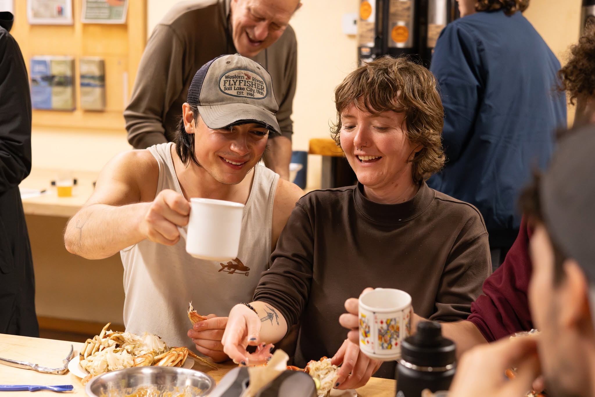 Two alumni cheers-ing their mugs while eating crabs